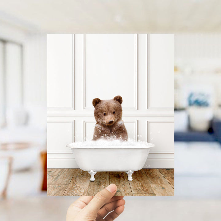 A brown bear sitting in a white bathtub filled with bubbles, with a blurred background suggesting a bathroom setting.
