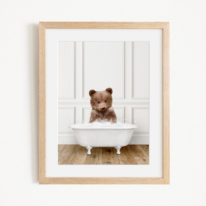 A small brown bear sitting in a white bathtub filled with water, creating a playful and adorable scene.