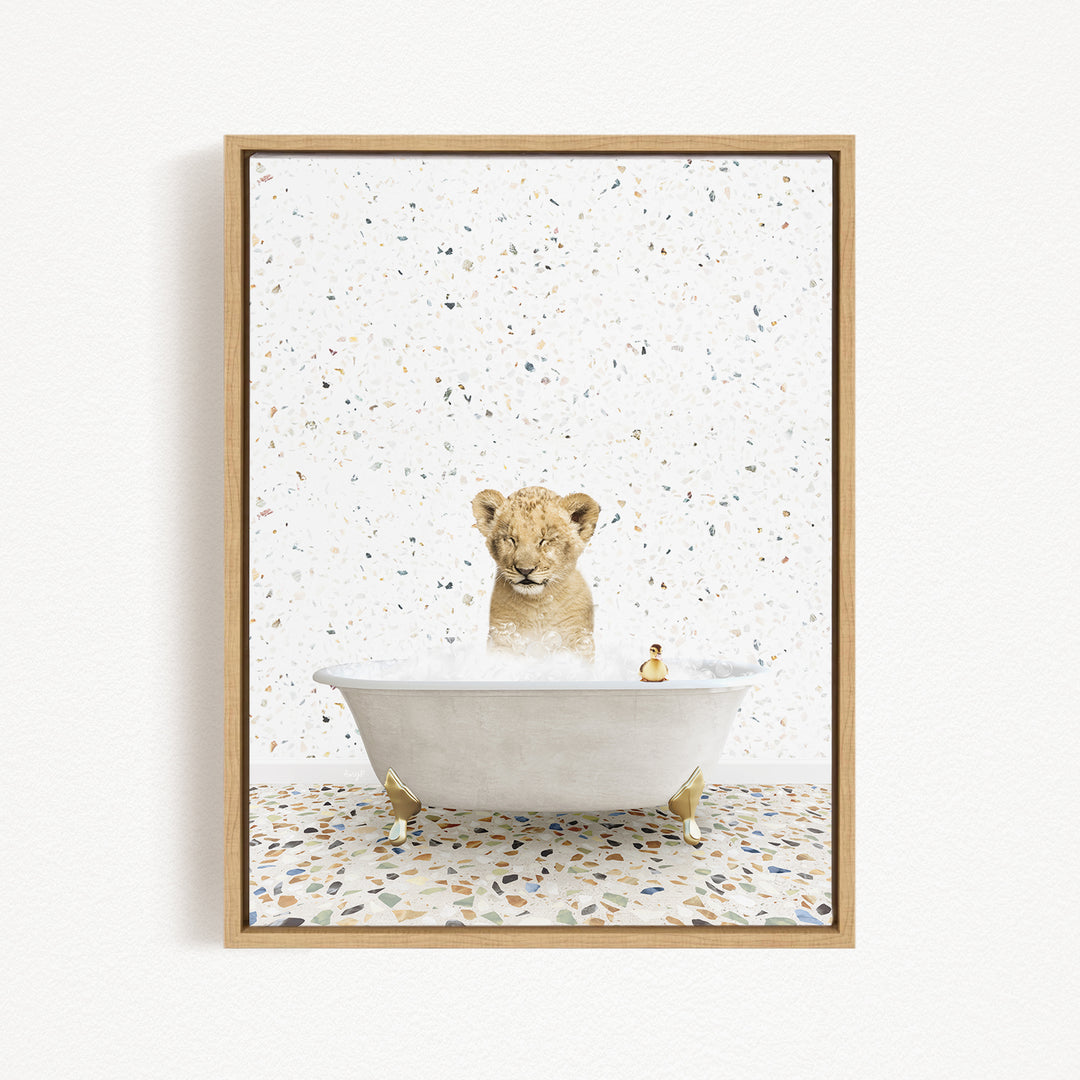 A young lion cub sitting in a white bathtub filled with bubbles, surrounded by a speckled tiled floor.