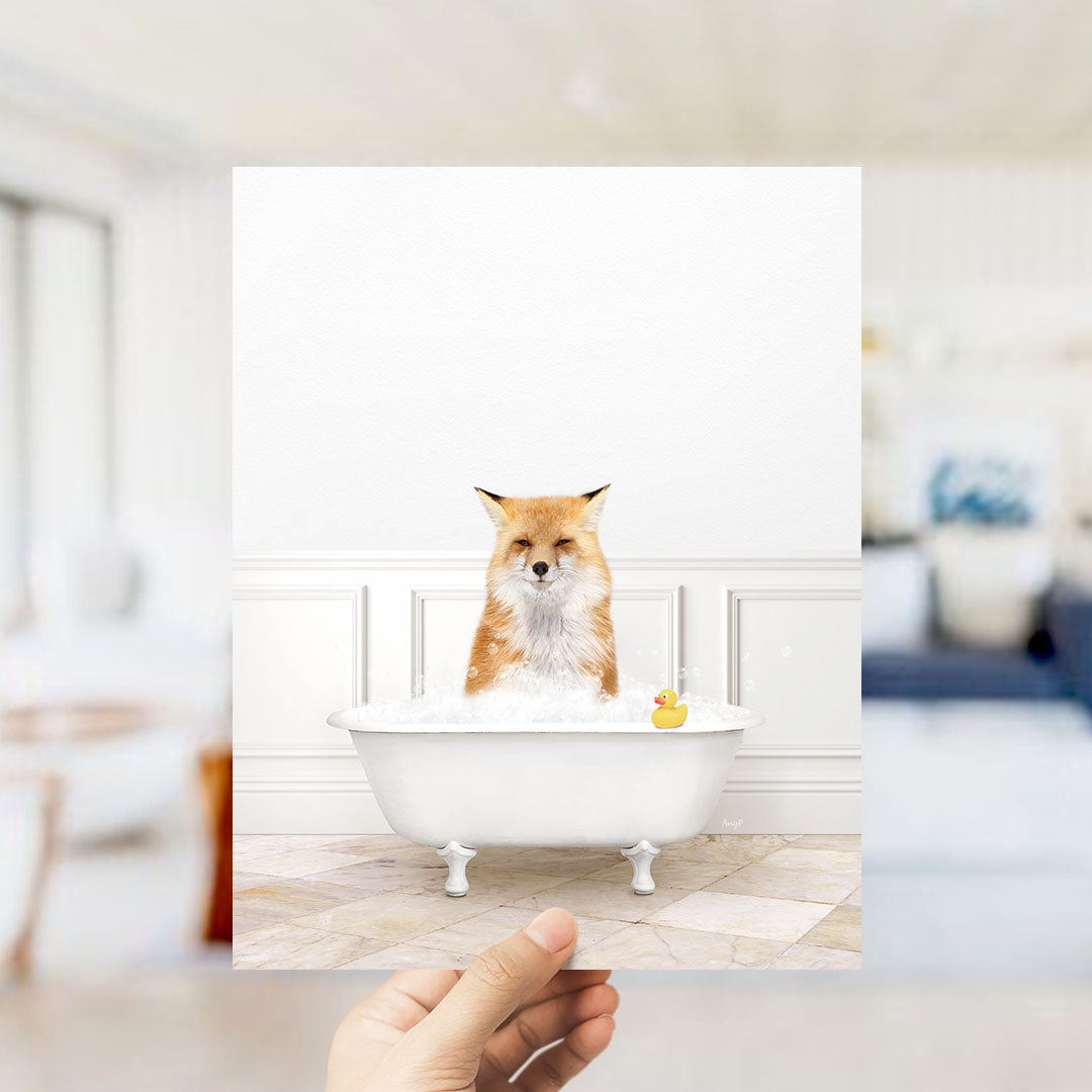 A hand holds up a framed image of a fox sitting in a bathtub filled with bubbles, with a rubber duck floating nearby.