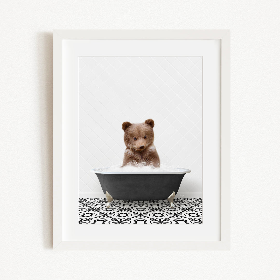 A cute brown bear cub sitting in a black bathtub filled with water, surrounded by a black and white patterned tile floor.