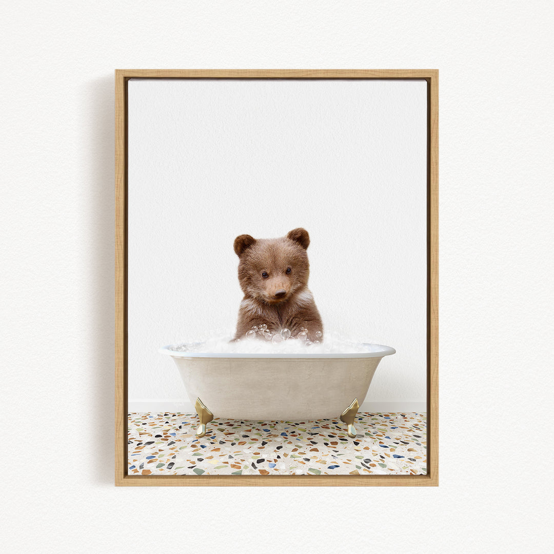 A cute brown bear cub sitting in a white bathtub filled with water, looking directly at the camera.