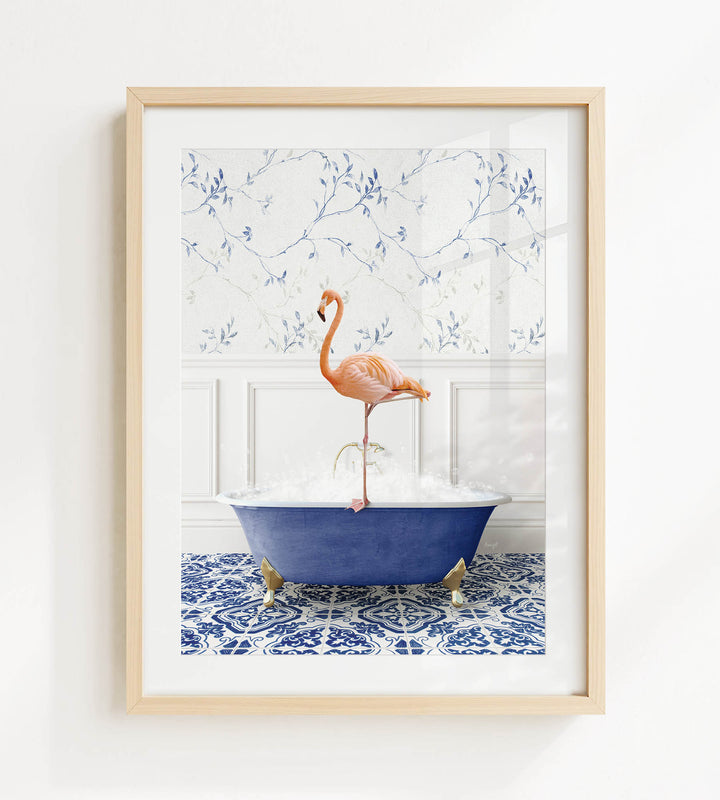 A framed image depicting a pink flamingo standing on the edge of a blue bathtub filled with bubbles, set against a blue and white floral wallpaper background.