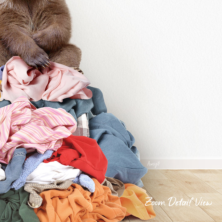 A pile of clothes, including various garments and linens, with a brown bear sitting atop the pile.