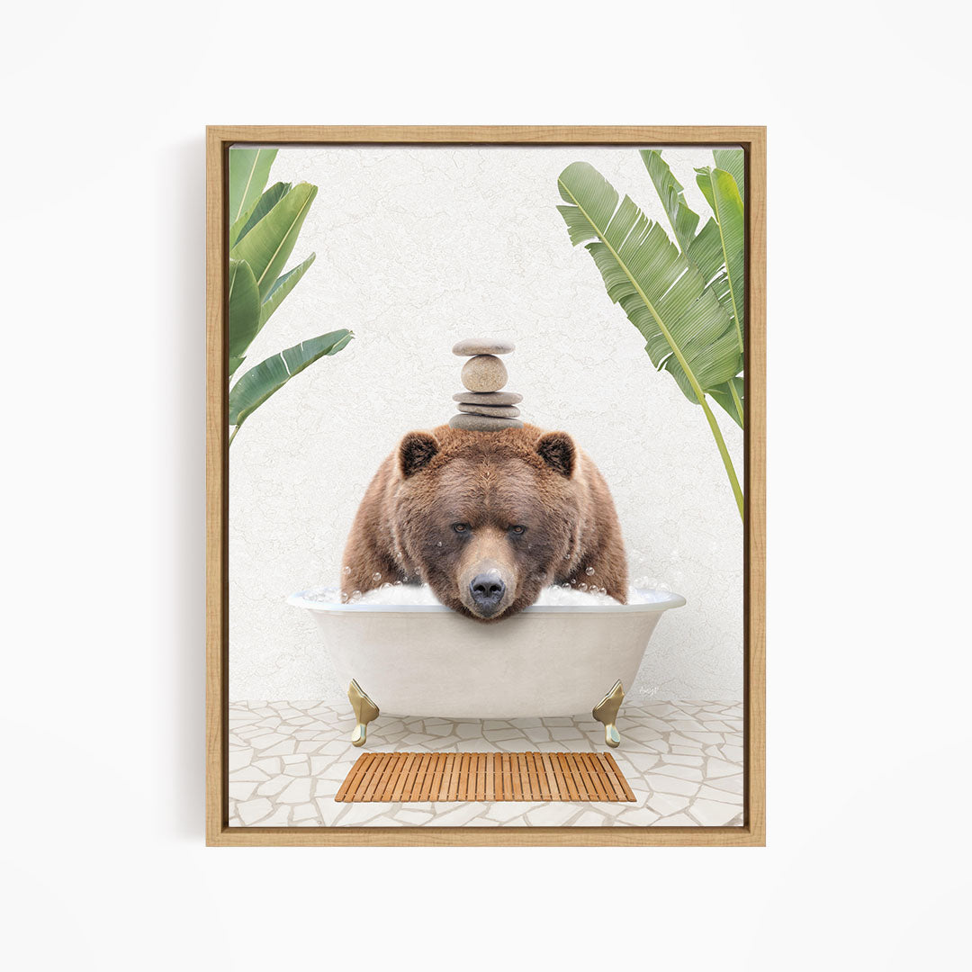 A brown bear is sitting in a white bathtub filled with water, surrounded by green leaves and a wooden mat on the floor.