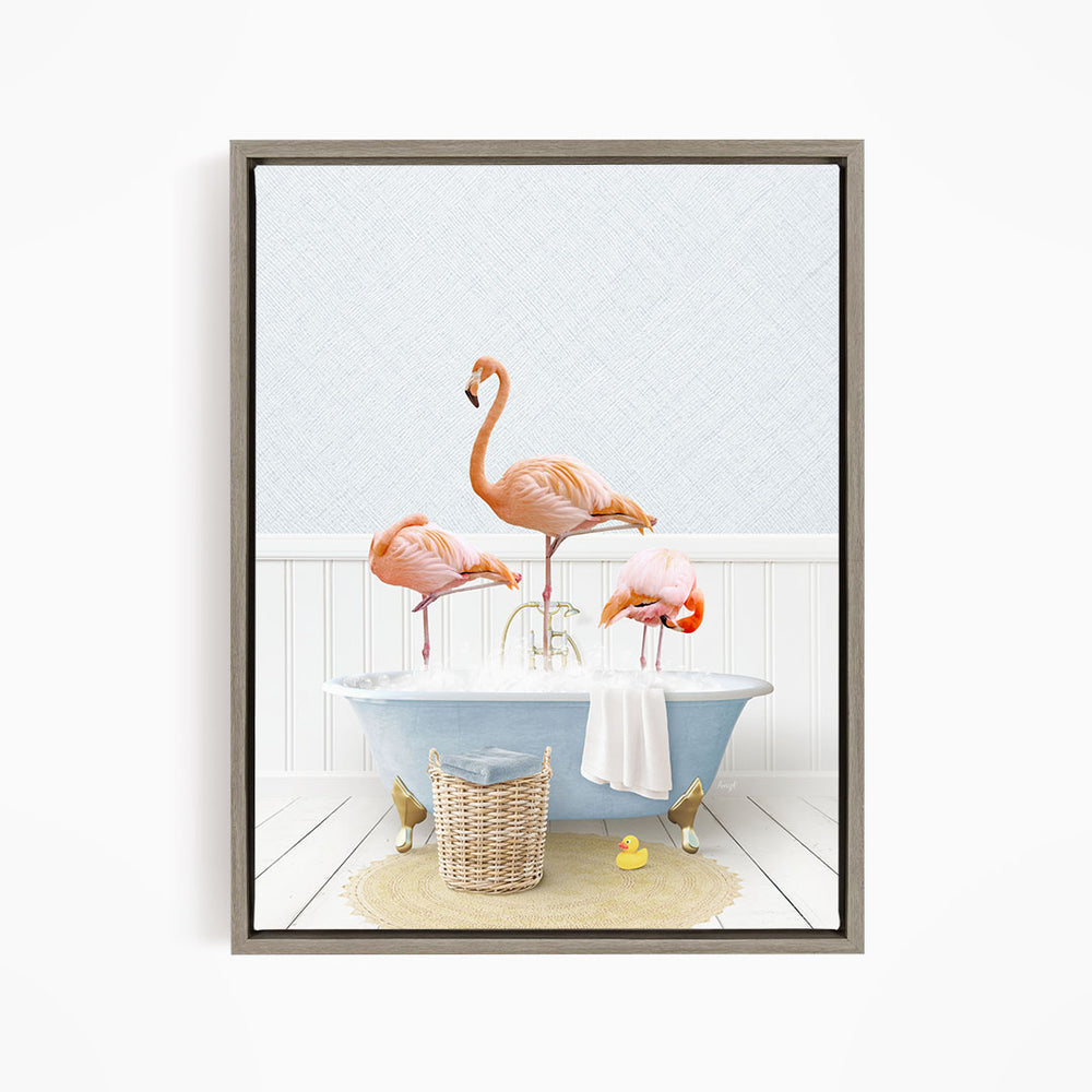 A framed image depicting three flamingos standing in a bathtub filled with water, surrounded by a basket of bath toys and a towel.