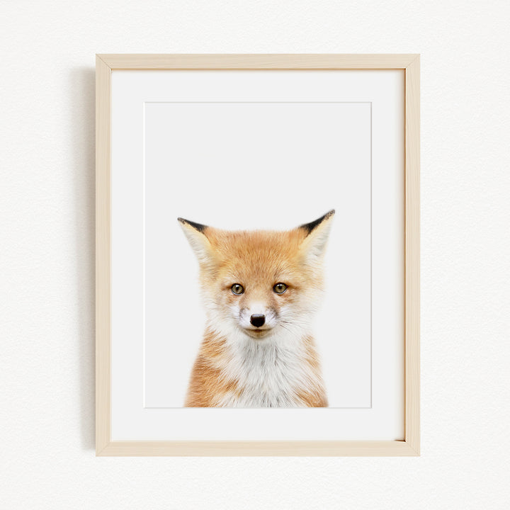 A framed print of a fox's face is displayed on a white wall.