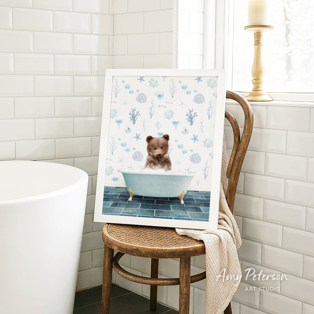 A framed image of a teddy bear sitting in a bathtub, surrounded by blue and white floral patterns, is displayed on a wooden chair in a bathroom setting.