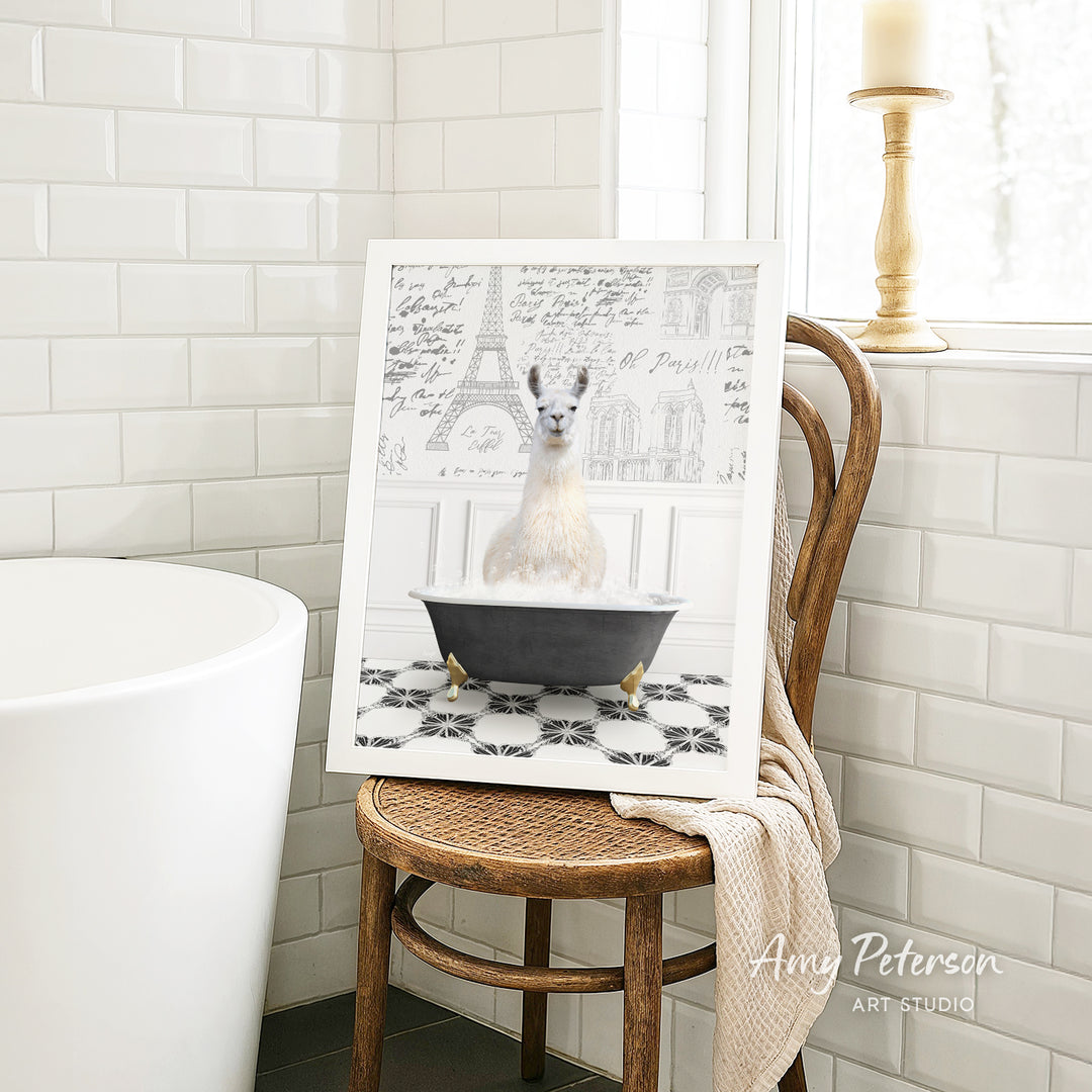 A framed image of a white llama sitting in a bathtub, surrounded by a tiled pattern, is displayed on a wooden chair in a bathroom setting.
