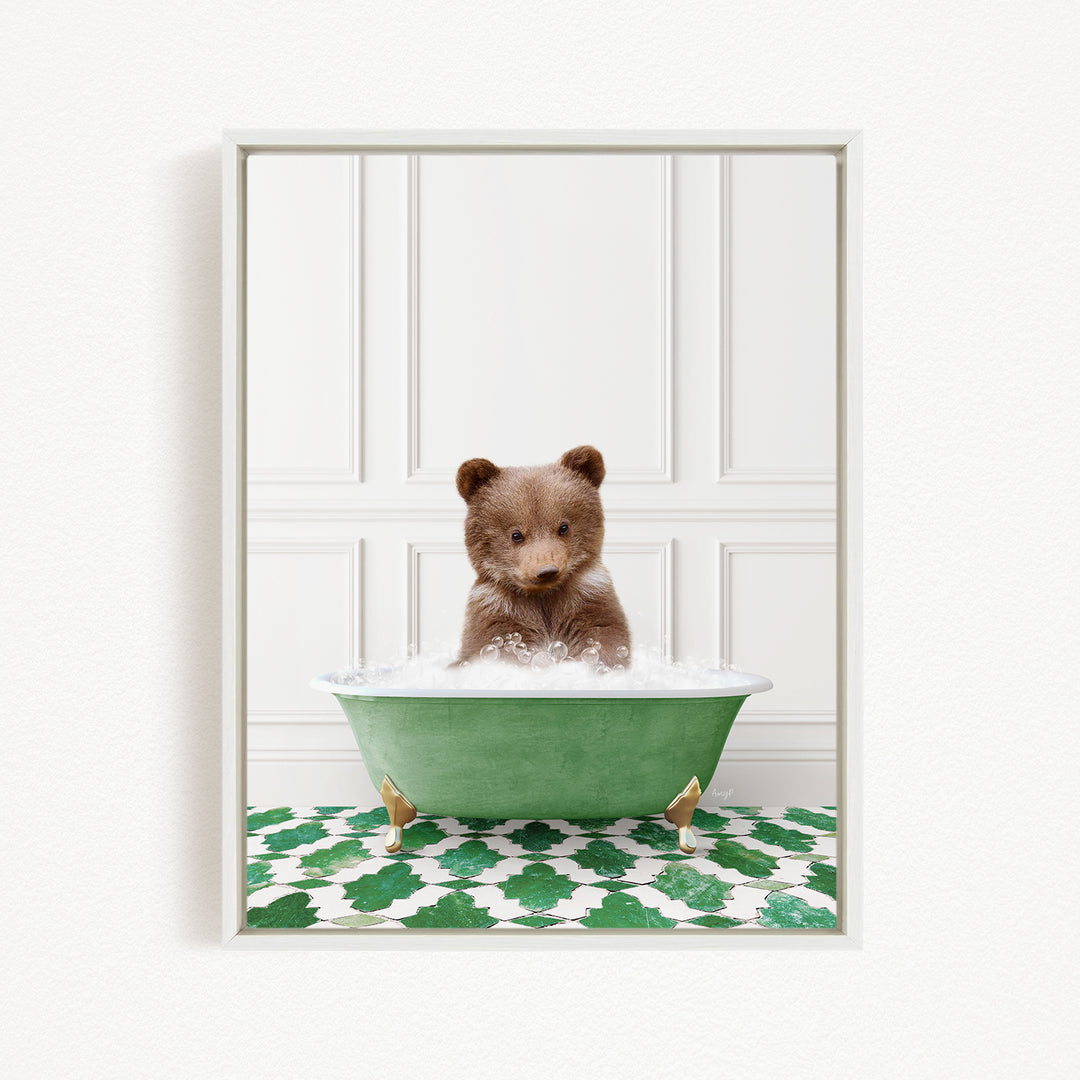A cute brown bear cub sitting in a green bathtub filled with bubbles, surrounded by a green and white patterned rug.
