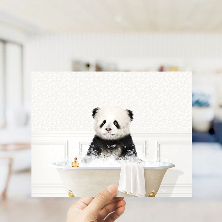 A hand holding a framed image of a panda bear sitting in a bathtub filled with bubbles.