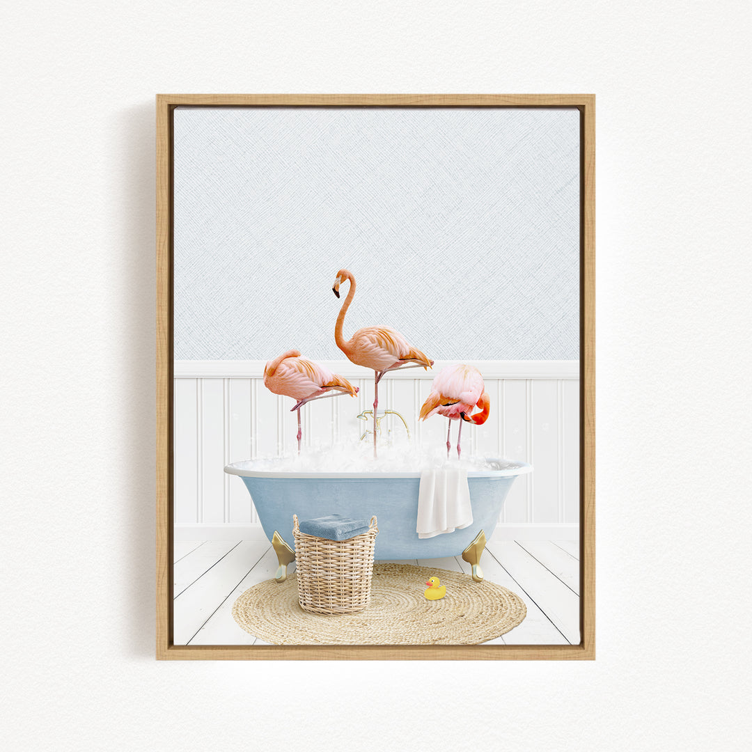A framed image depicting three flamingos standing in a blue bathtub filled with bubbles, surrounded by a basket of bath toys and a yellow rubber duck.