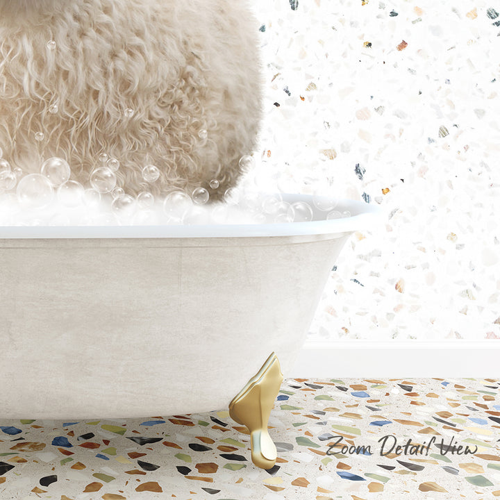 A fluffy white dog is sitting in a white bathtub filled with bubbles, with a mosaic floor in the background.