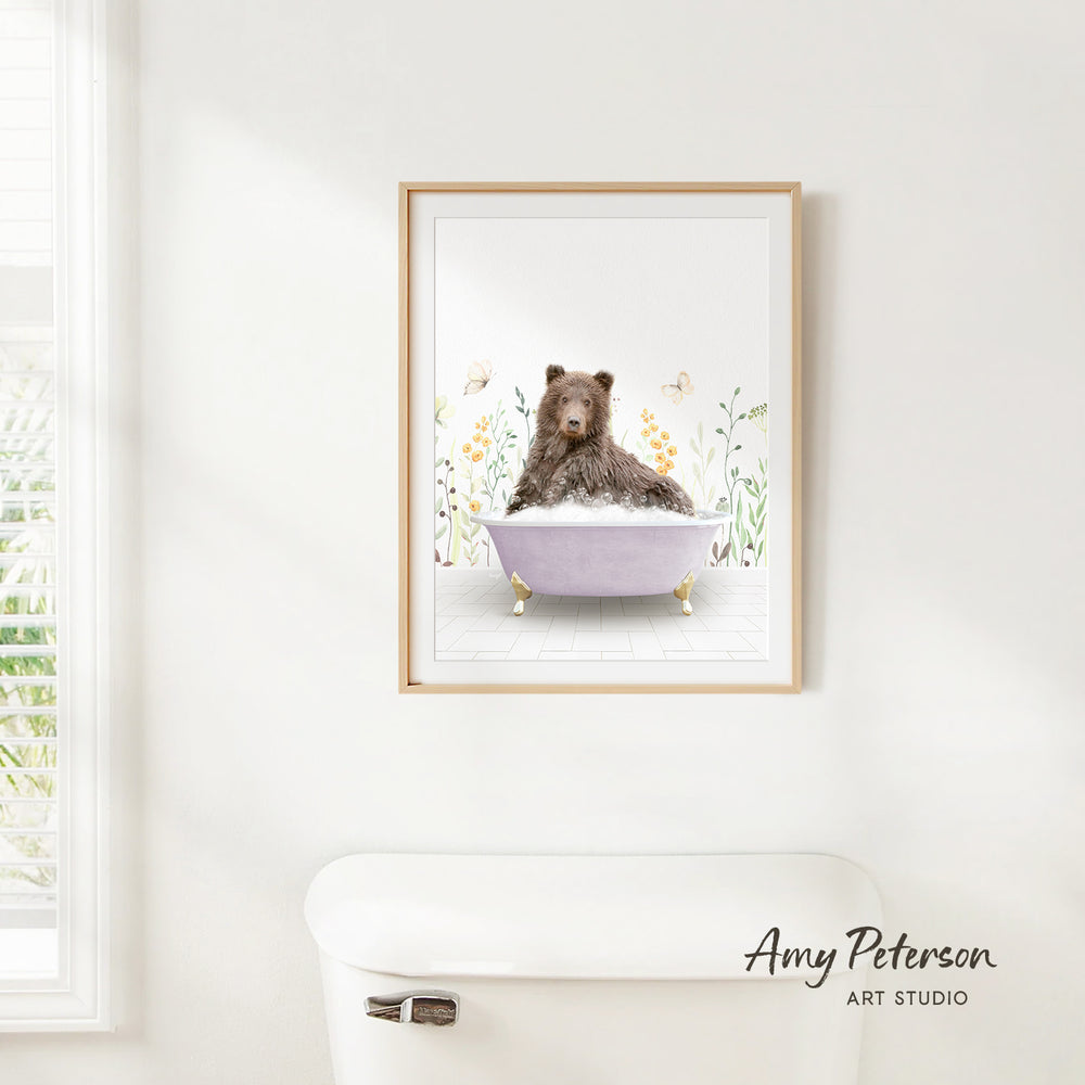 A framed print of a brown bear sitting in a bathtub, surrounded by flowers and butterflies, hangs on a white wall.