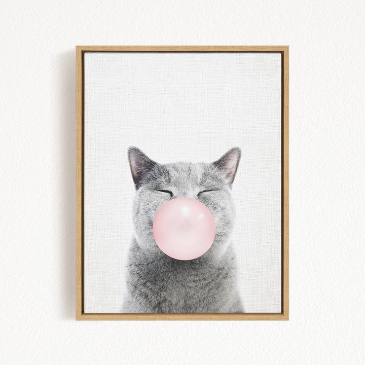 A gray cat blowing a pink bubble with its mouth.