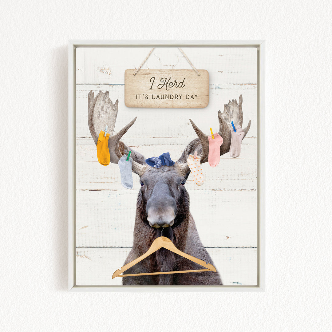 A framed image depicting a moose with a sign above it that says "I herd, it's laundry day".