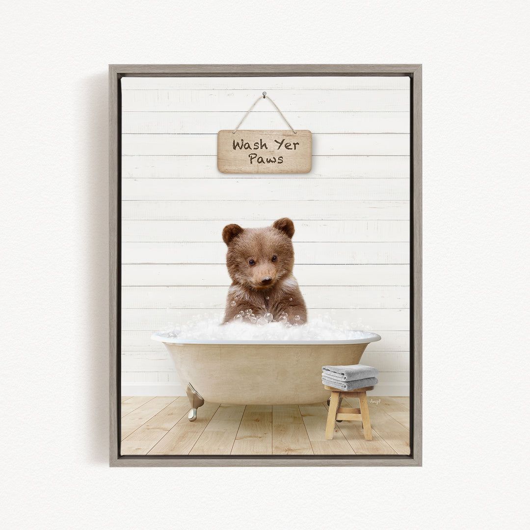 A cute brown bear sitting in a bathtub filled with water, with a sign above that says "Wash Yer Paws".