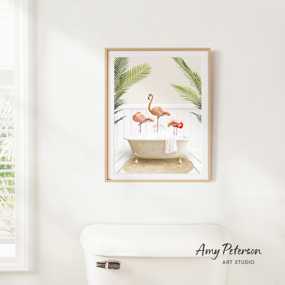 A framed print of a pink flamingo standing in a bathtub, surrounded by green palm leaves, hangs on a white wall in a bathroom.