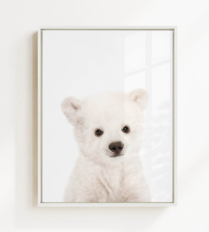 A cute white polar bear cub with large eyes and a black nose is the focus of the image.