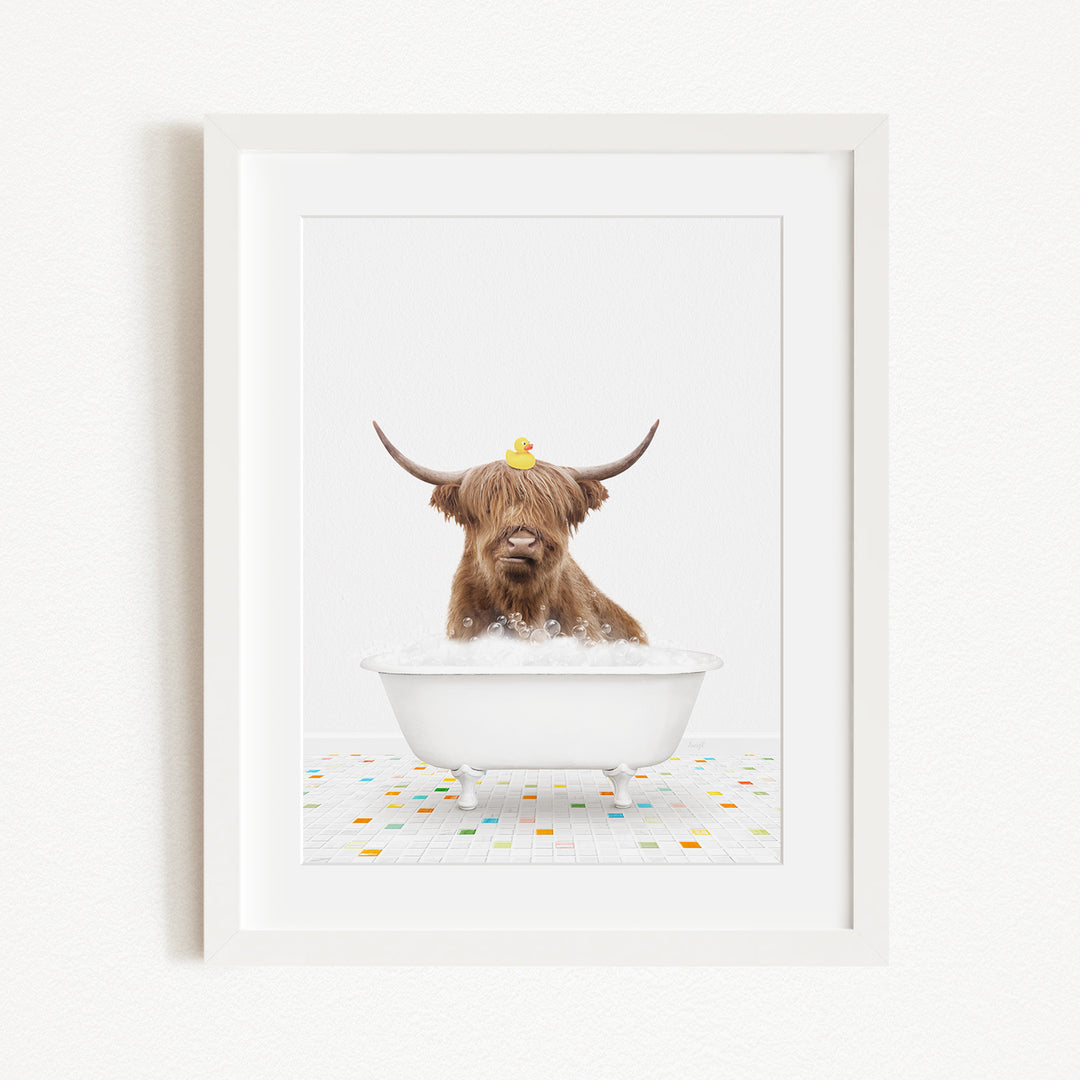 A brown cow with long horns is sitting in a white bathtub filled with bubbles, with a yellow rubber duck perched on its head.