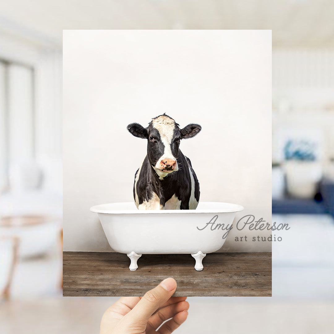 a hand holding up a photo of a cow in a bathtub