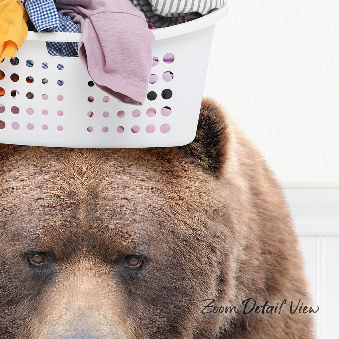 A close-up of a brown bear's face peering over a laundry basket filled with clothes.