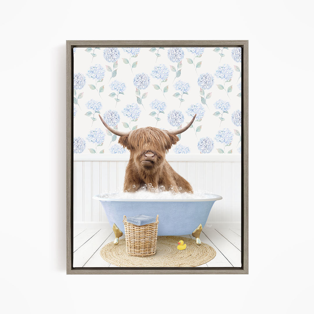 A brown cow with long horns is sitting in a blue bathtub filled with water, surrounded by a wicker basket and yellow rubber ducks.