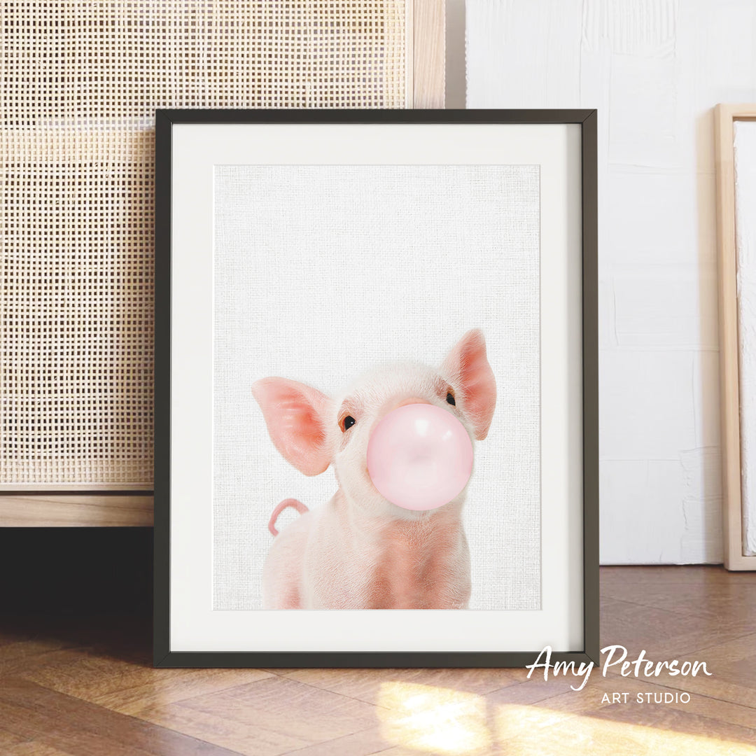 A framed photograph of a cute pig blowing a bubble with a pink bubblegum bubble.