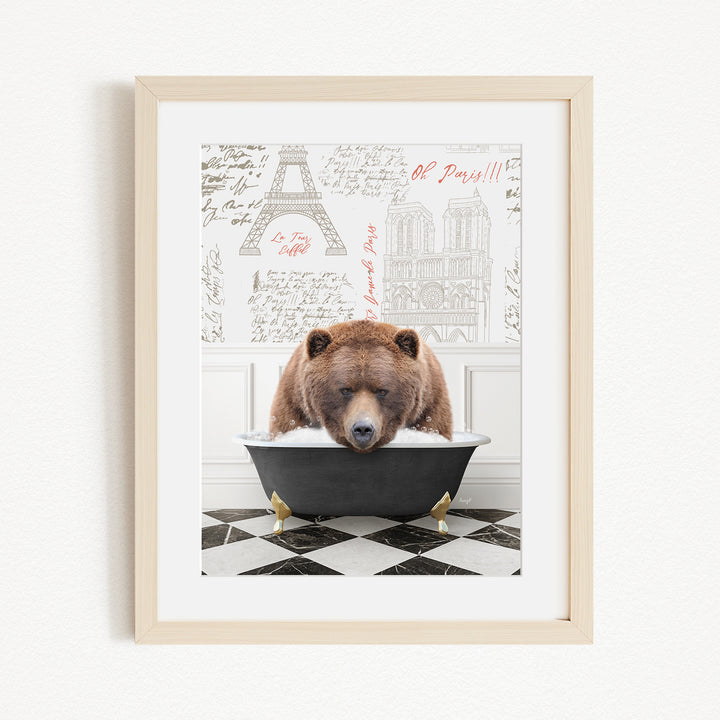 A framed image depicting a brown bear sitting in a bathtub, with a Paris-themed background featuring the Eiffel Tower and other Parisian landmarks.