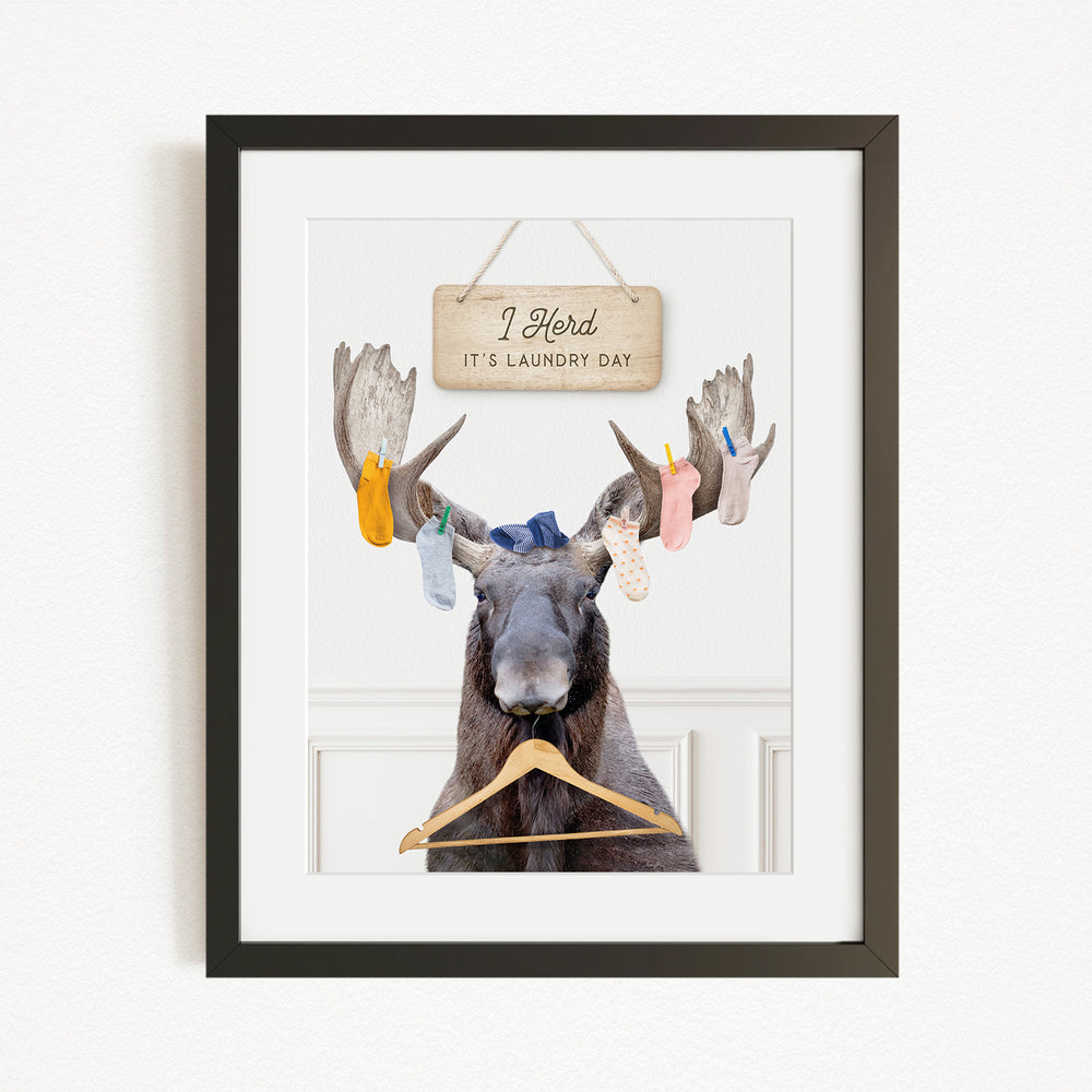 A framed image depicting a moose with a sign above it that says "I herd it's laundry day".