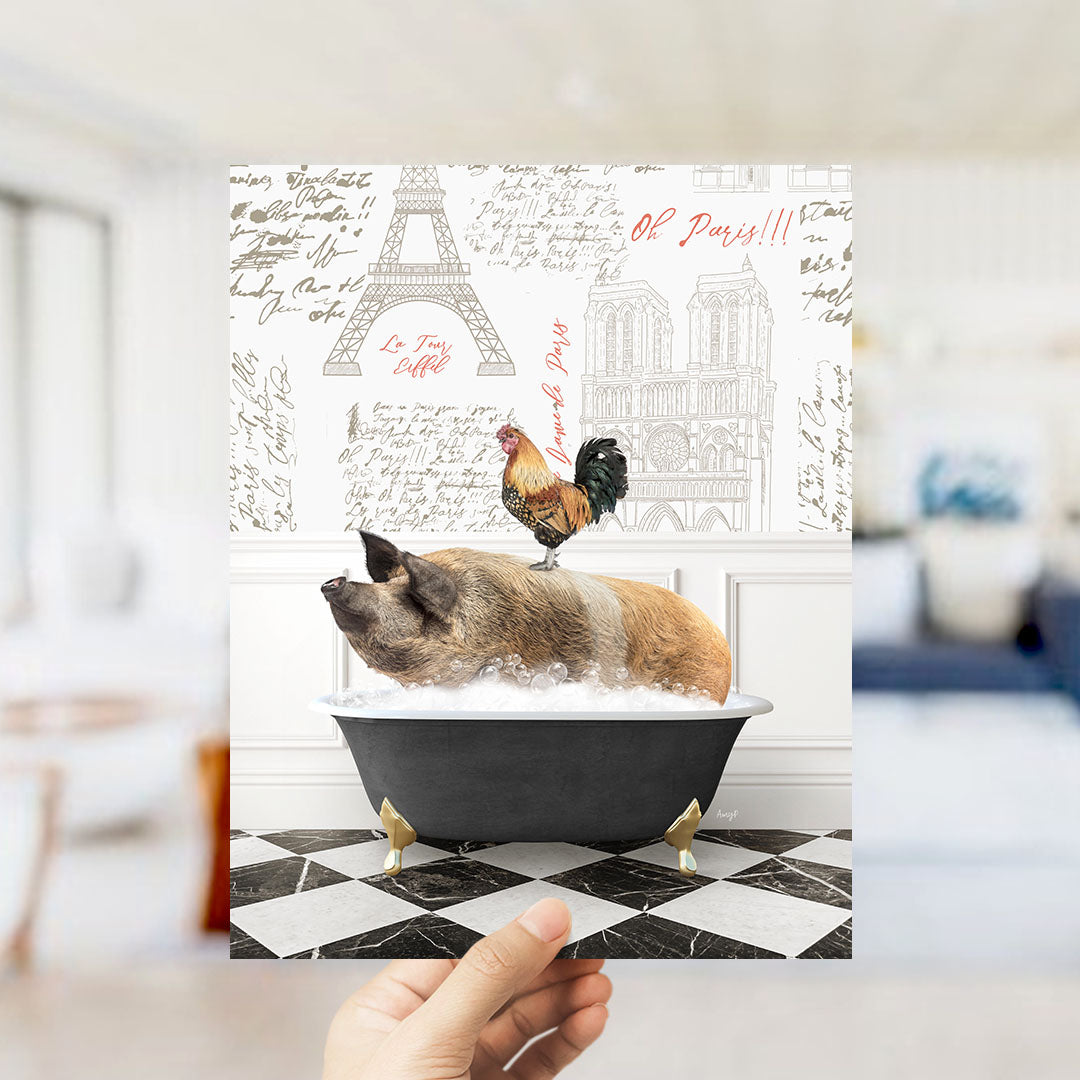 A hand holds up a printed image featuring a pig sitting in a bathtub, with a rooster perched on its back, against a backdrop of the Eiffel Tower and Parisian architecture.