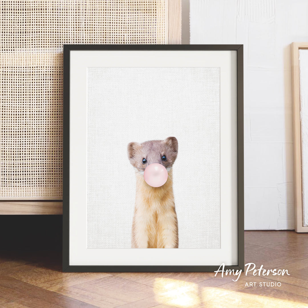 A framed photograph of a small animal, possibly a rodent, blowing a bubble with a pink bubble gum bubble.