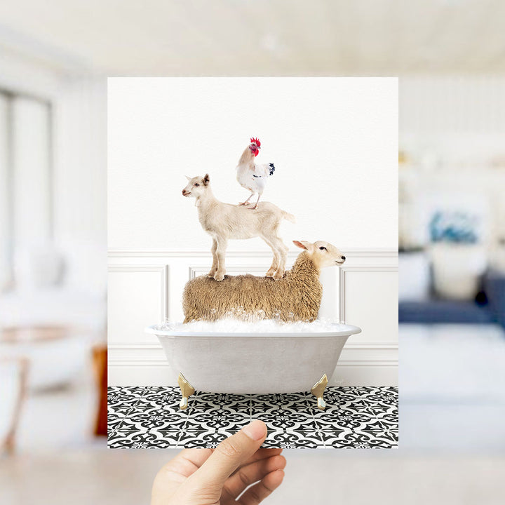 A hand holds up a framed image depicting a goat standing on a sheep's back in a bathtub, with a rooster perched on top of the sheep.