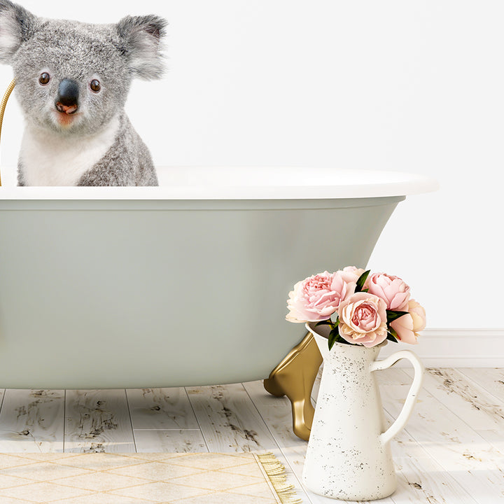 A koala sitting in a bathtub, with a vase of pink flowers next to it on a wooden floor.