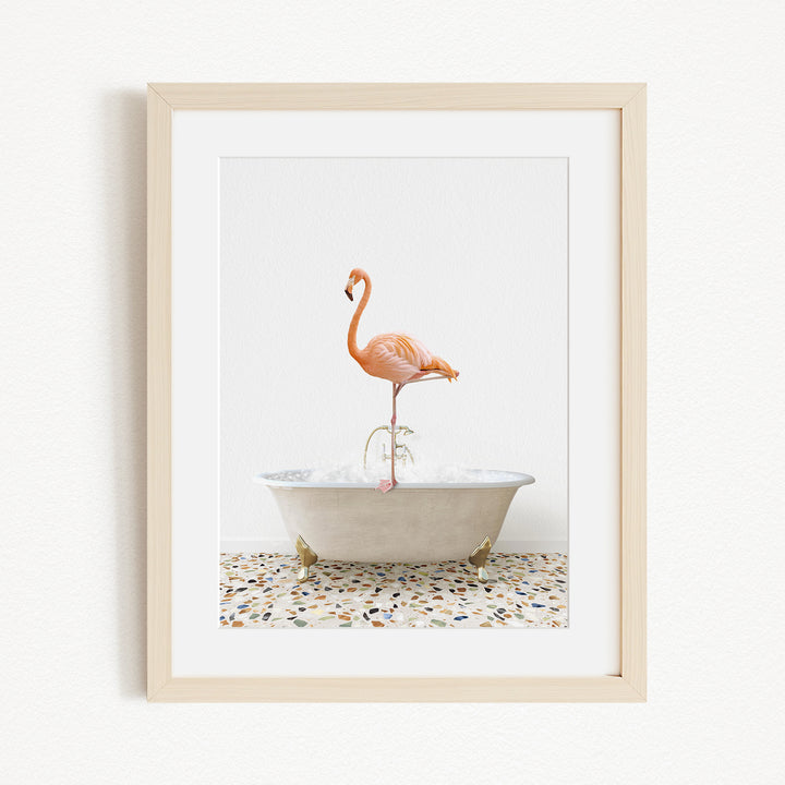 A framed image of a pink flamingo standing on one leg in a white bathtub filled with water.