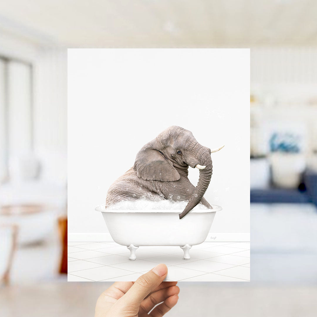 A gray elephant sitting in a white bathtub filled with bubbles, with a blurred background suggesting a bathroom setting.