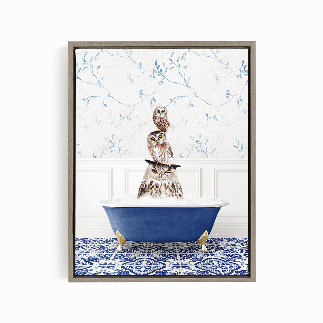 A framed image depicting a group of owls sitting in a blue bathtub, with a patterned tile floor and a floral wallpaper in the background.