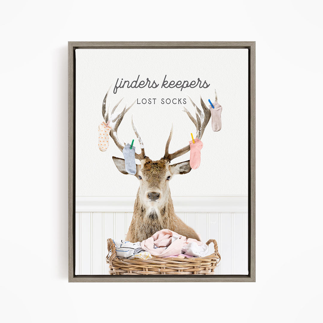A deer with antlers holding up socks in a basket, with the text "finders keepers" and "lost socks" above the deer.