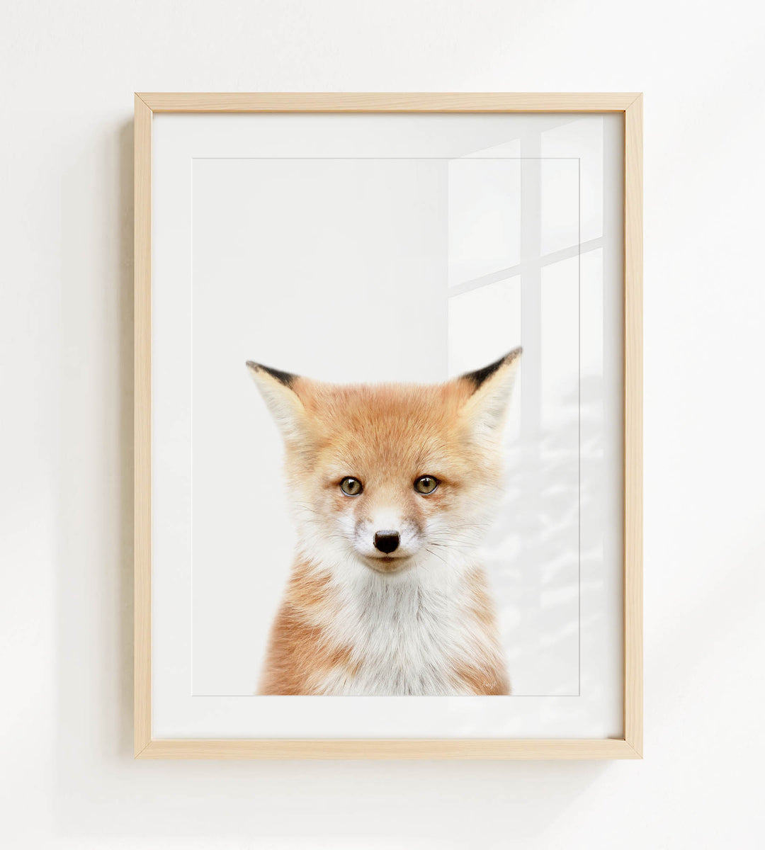 A framed print of a fox's face is displayed on a white wall.