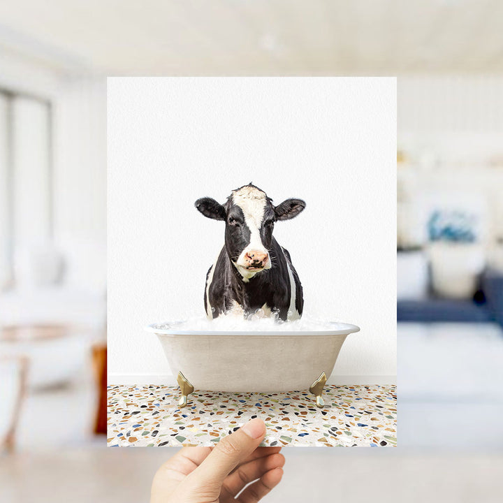 A black and white cow is sitting in a white bathtub filled with water, creating a humorous and unexpected scene.