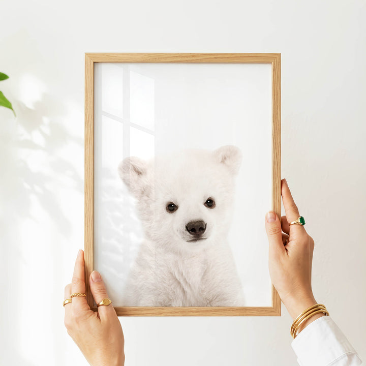 A person's hands are holding a wooden frame with a picture of a cute white polar bear inside it.
