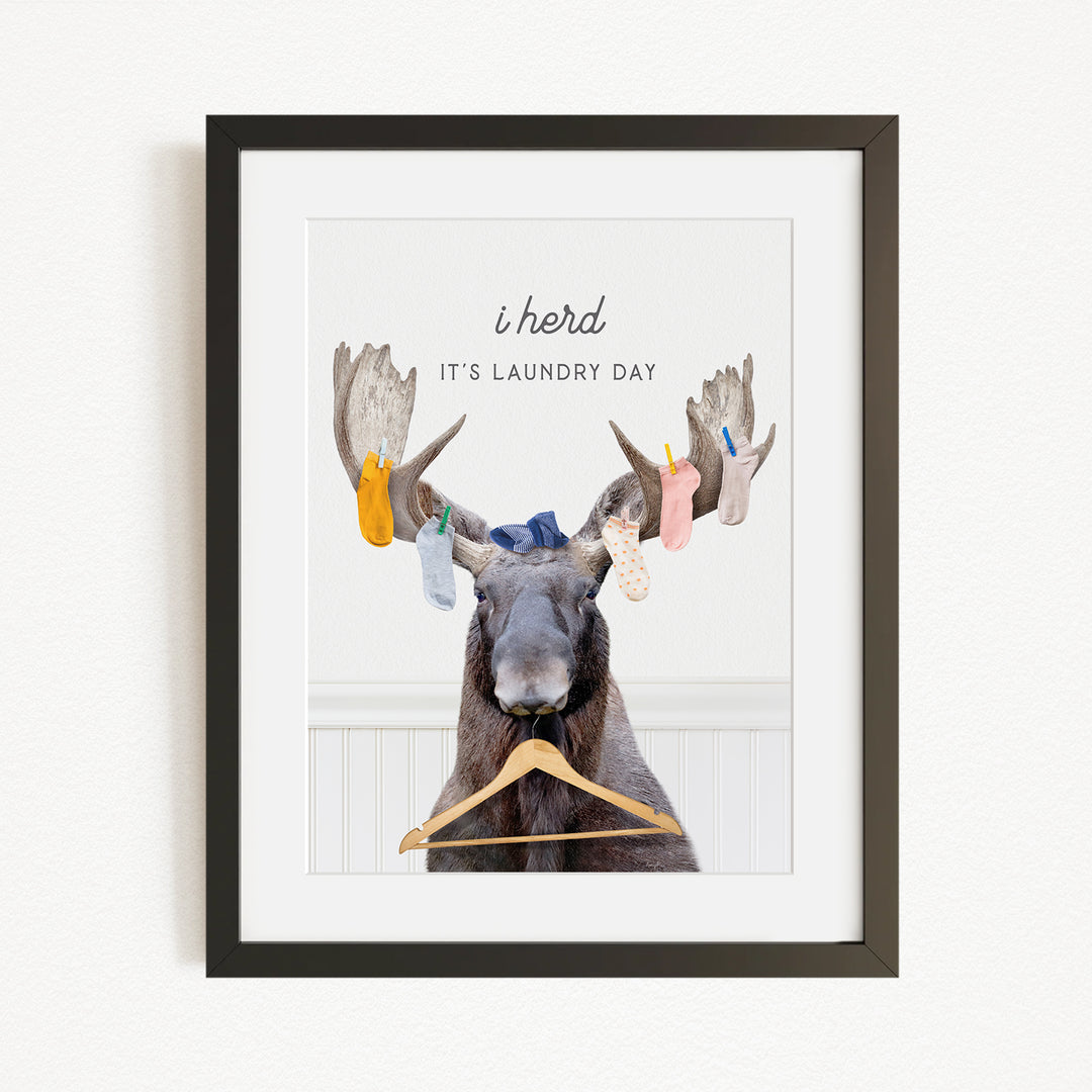 A framed image depicting a moose with a laundry basket hanging from its antlers, accompanied by the text "It's laundry day"