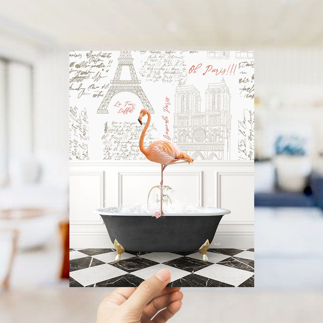 A hand is holding up a print featuring a pink flamingo standing on a black bathtub, with a wall decorated with the Eiffel Tower and other Parisian landmarks in the background.