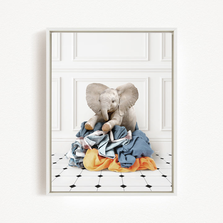 A stuffed elephant toy is sitting on a pile of clothes on a tiled floor.