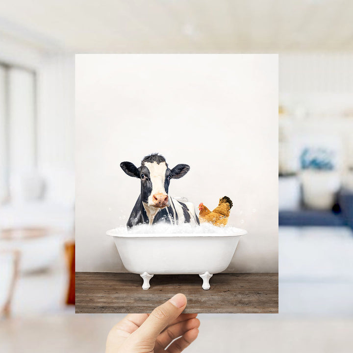 A hand holds up a framed image of a cow and a chicken sitting in a bathtub filled with water.