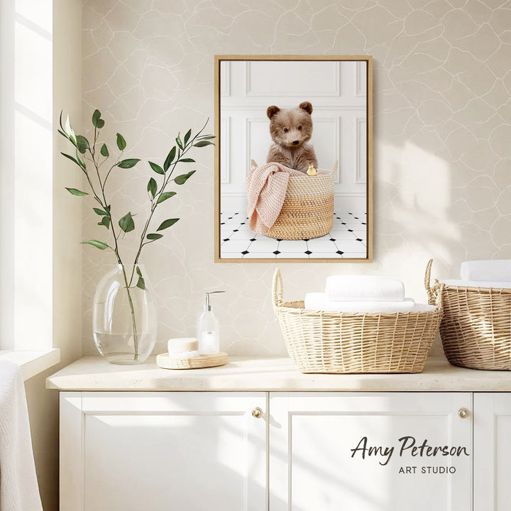 a framed photograph of a bear sitting in a basket, placed on a wall above a white cabinet with two woven baskets on top.