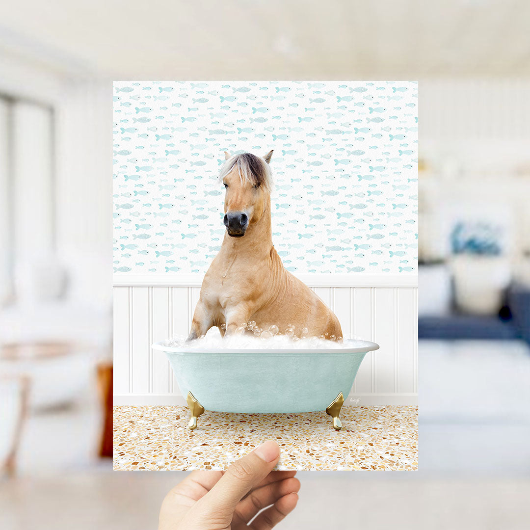 A hand holds up a framed image of a horse sitting in a bathtub filled with bubbles, surrounded by a pattern of small fish.