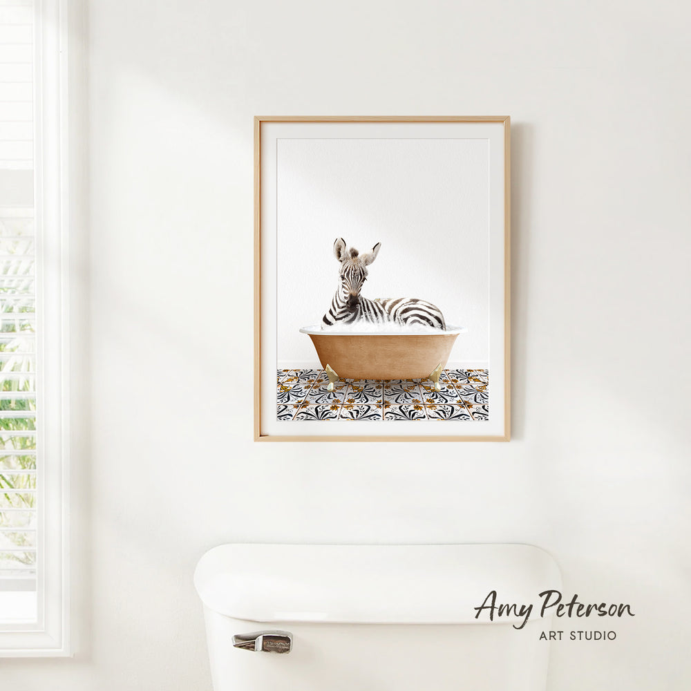 A framed print of a zebra resting in a bathtub is hanging on a white wall in a bathroom.