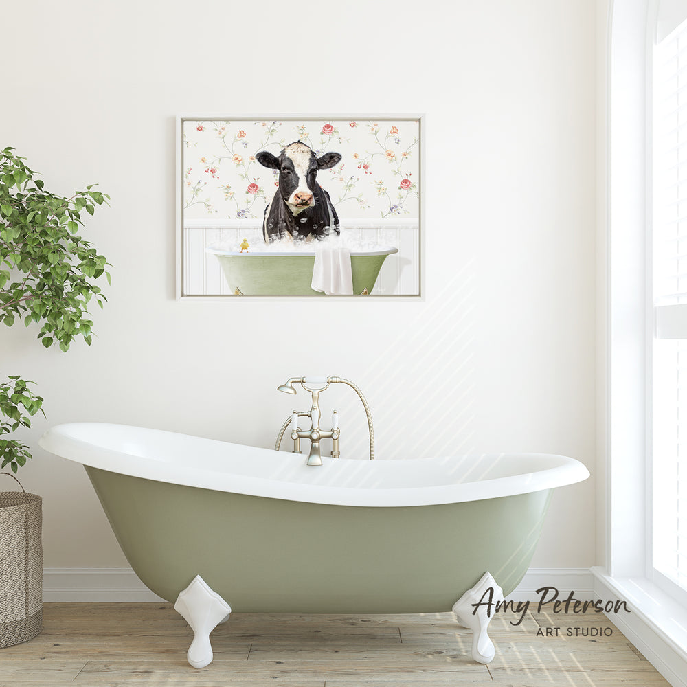 A green clawfoot bathtub with a framed cow image above it, set against a white wall with a window and a potted plant.