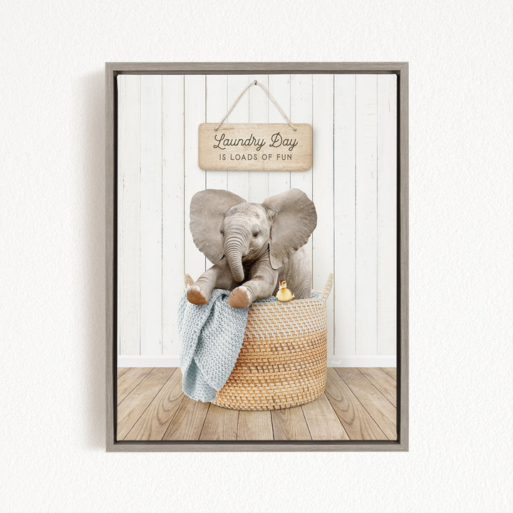 A gray elephant sitting in a woven basket, with a sign above that says "Laundry Day is loads of fun".